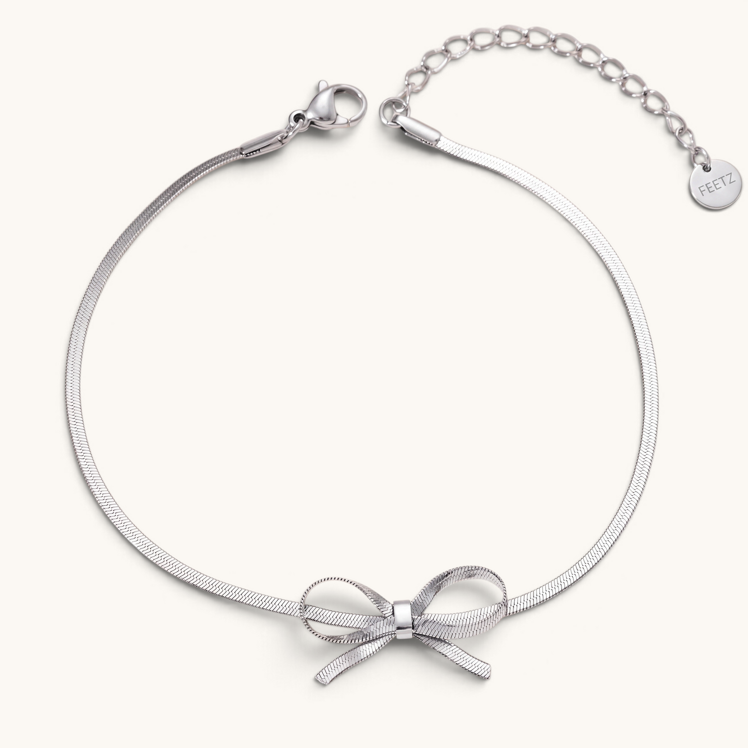 Feetz & Co. Eterna silver herringbone chain anklet featuring a delicate bow charm in polished stainless steel.