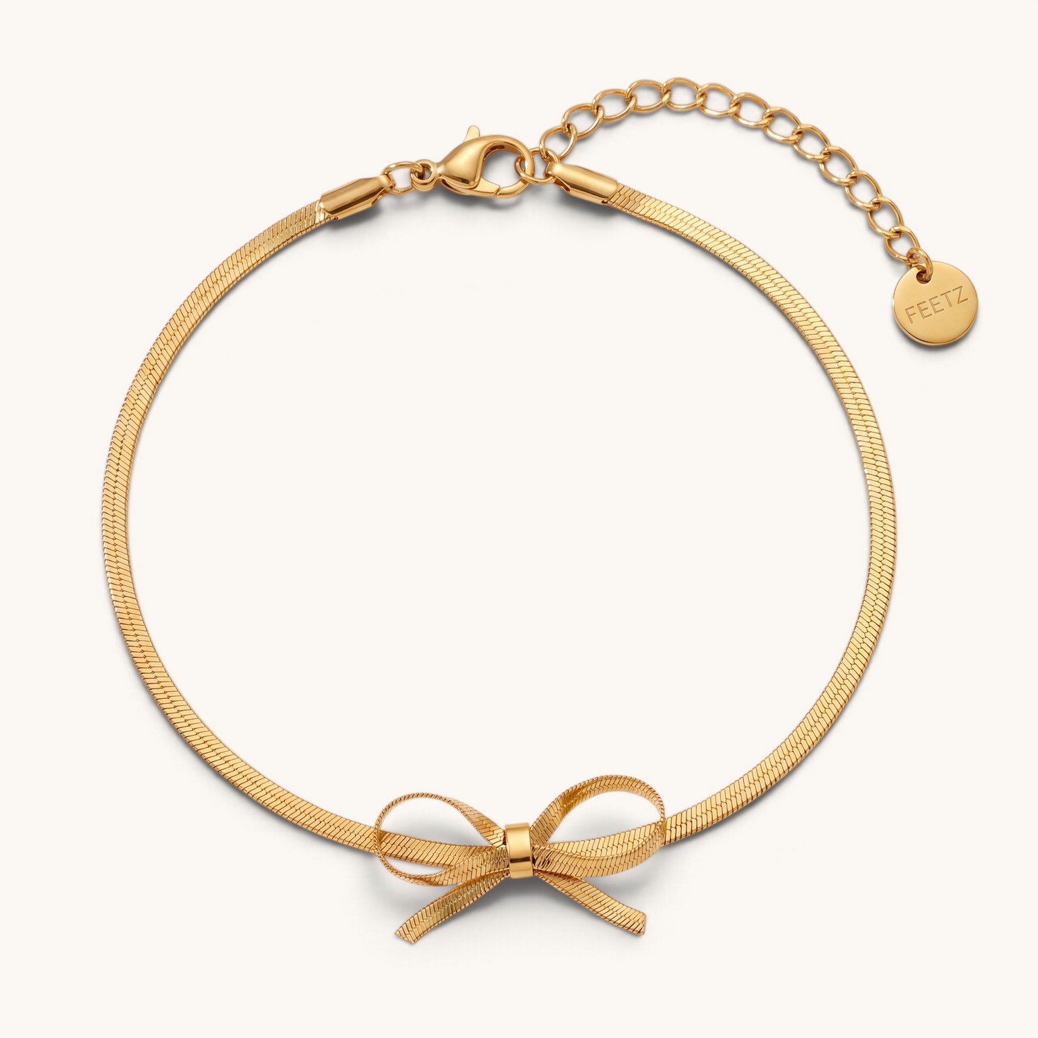 Feetz & Co. Eterna gold herringbone chain anklet featuring a delicate bow charm and adjustable lobster clasp closure.