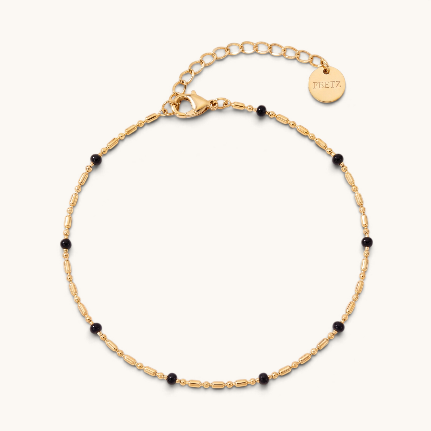 Feetz & Co. Onice anklet featuring a gold-tone stainless steel chain with small black beads and a branded charm.