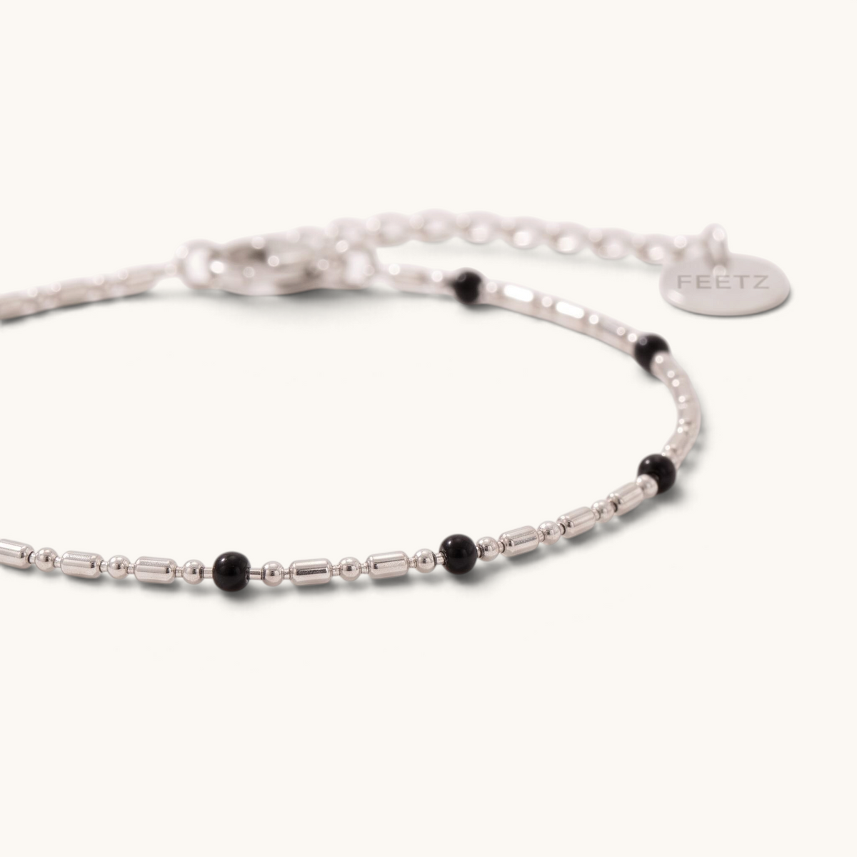 Feetz & Co. Onice anklet featuring a fine silver-tone stainless steel chain with small black beads and a logo tag.
