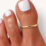 Feetz & Co. gold-plated stainless steel open band big toe ring on a foot with white nail polish